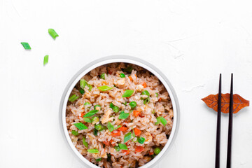 Fried rice with vegetables and egg in the gray ceramic bowl on the white table. Chinese food. Copy space