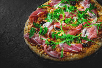Pizza with Mozzarella cheese, ham, pepper, olive, meat, Tomato sauce, Spices and Fresh arugula. Italian pizza on black plate on Dark grey black slate background