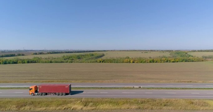 A truck with a red container is driving along the road. A truck with an orange cabin transports a red container view from a drone