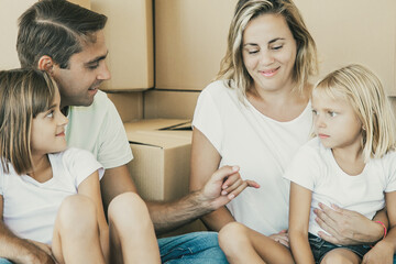 Caucasian family in new apartment or house. Parents holding kids. Father giving promise to his daughter. People surrounded carton boxes during relocation. Mortgage, relocation and moving day concept