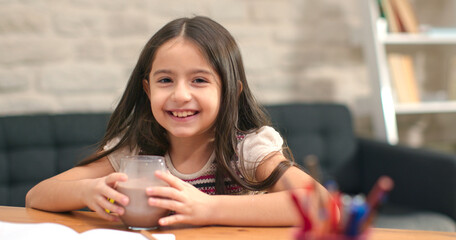 Little girl taking a break from studying, laughing, looking at the camera. Drinking cocoa milk....
