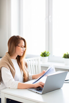 Online work concept. Vertical photo of a woman works online in front of a laptop monitor. She fills out tax forms or pays bills. Photo in home interior.
