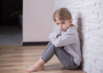 angry little girl sitting on a floor at home.