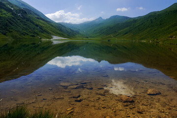 stones on the ground of a clear mountain lake with green mountains around
