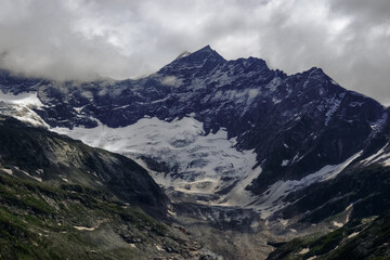 snow and a huge glacier on rocky mountains with clouds