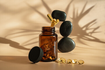 Obraz na płótnie Canvas The pills fall into the jar. Levitation style. Omega 3 tablets on a beige background. Black stones for acapuncture