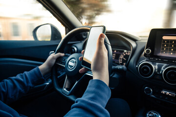 Fototapeta na wymiar Teen drive a car and use smartphone. Young man reading messages holding a cell phone while driving. Dangerous behavior, accident risk. Danger, transgression, youth, distraction concept. Focus on hand.