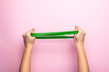 Female hands doing exercise with fitness rubber bands on a pink background. Home gym concept, copy space, minimal, trendy backdrop.