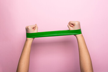 Female hands doing exercise with fitness rubber bands on a pink background. Home gym concept, copy space, minimal, trendy backdrop.