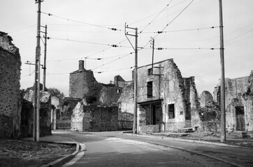 Aftermath of war shows ruined buildings and tram lines in Oradour-sur-Glane in France. This historic village is now a memorial to those who died in WW2. Monochrome image. Empty road with tram lines.