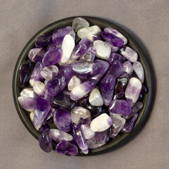 Set of various amethyst natural mineral stones and gemstones on grey linen and black plate...