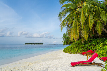 Strand mit Palmen und einer Sonnenliege auf den Malediven, im Hintergrund eine kleine Insel umgeben von türkisem Wasser