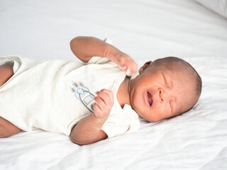 African American baby boy crying on a white bed.