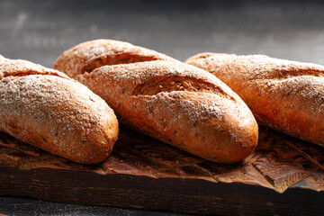 Three loafs of fresh baked baguette on the wooden cutting board on gray background