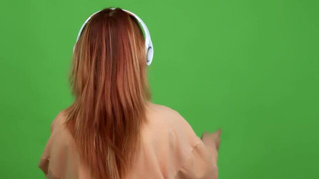 Teenager girl listening music with headphones pointing back with the index finger over isolated background