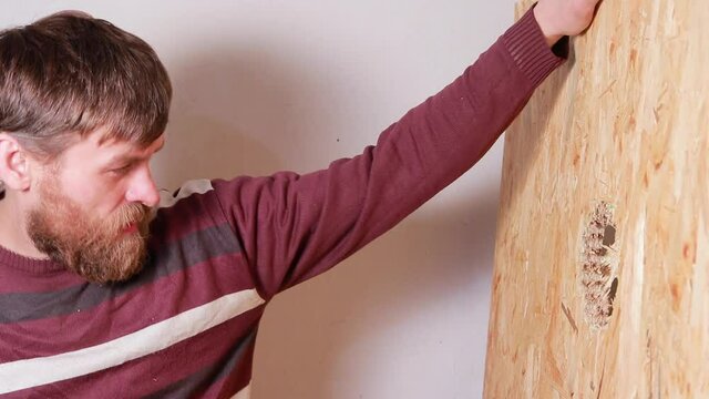 A male carpenter punches a hole in the chipboard with a hammer. Construction work, home repair yourself