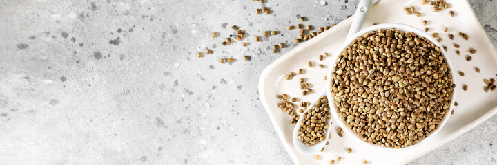 Hemp seeds. Peeled and whole dried hemp seeds in a white ceramic bowl on a light gray kitchen table. Hemp Seeds for Cooking	