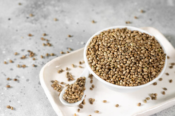 Hemp seeds. Peeled and whole dried hemp seeds in a white ceramic bowl on a light gray kitchen table. Hemp Seeds for Cooking