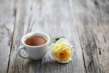 small tea cup and yellow rose on wooden table