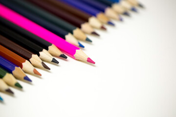A pink coloring pen sticking out of other darker color pencils to depict being different and leadership.