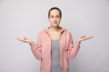 The pretty and grown-up girl spread her hands uncomprehendingly, isolated against the white background. An attractive young lady with dark brown hair in a pink bike looks worried.