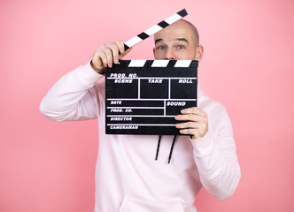 Young bald man wearing casual sweatshirt over pink isolated background holding clapperboard very...