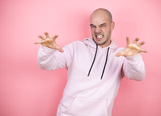 Young bald man wearing casual sweatshirt over pink isolated background smiling funny doing claw...
