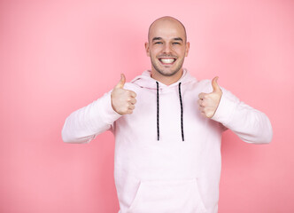 Young bald man wearing casual sweatshirt over pink isolated background smiling and doing the ok signal with his thumbs