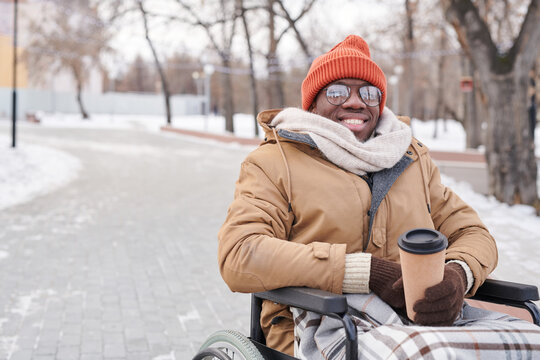 Portrait of African disabled man in wheelchair smiling at camera while drinking hot coffee in the park
