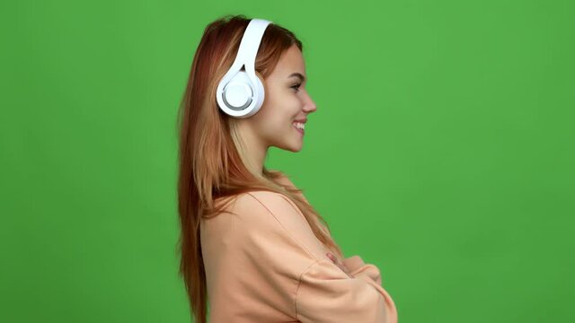 Teenager girl listening music with headphones looking side over isolated background