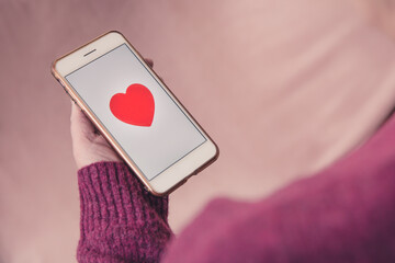 Girl using a touchscreen with a romantic love heart massage to find love and relationship on an online dating app - obrazy, fototapety, plakaty