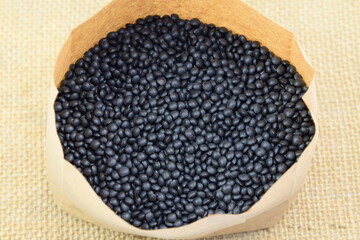 Black lentil, beluga lentil in paper bag on jute fabric backgroundcloseup