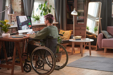 Rear view of disabled woman working as a programmer on computer with new software in domestic room