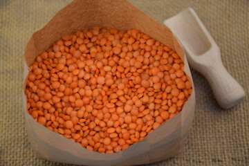 Red lentil in paper bag on jute fabric background wooden spoon blurred