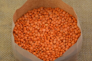 Red lentil in paper bag on jute fabric background