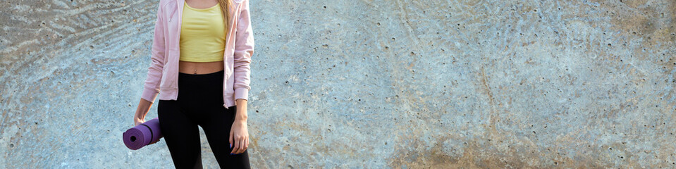 Obraz premium A sporty slim girl in leggings and a top is standing with a training mat, resting between exercises.