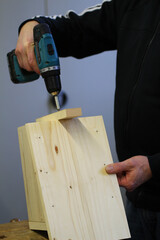 Eine Hand h&auml;lt einen Akkuschrauber und schraubt helles Holz zusammen