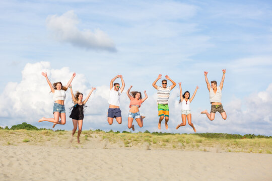 Multiethnic group of friends jumping together at seaside - Happy people enjoying summer time together after lockdown - Achievement and success concepts