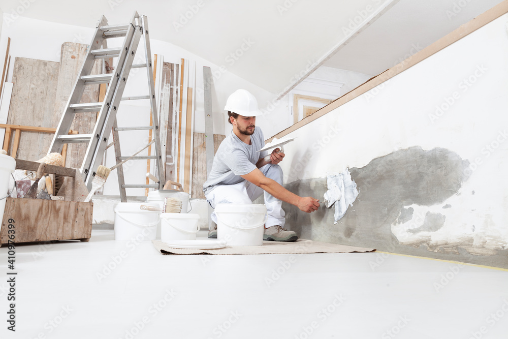 Wall mural man plasterer construction worker at work, takes plaster from bucket and puts it on trowel to plaste