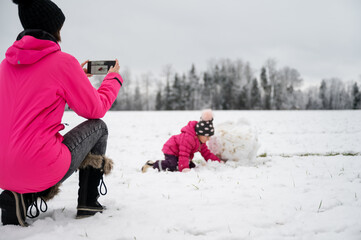 Fototapeta na wymiar Mother taking photo of child playing in snow