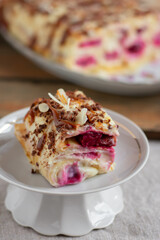 Cake from rolled pancakes with custard, cherries and grated chocolate on white plate, on a light background. Selective focus.