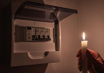 Housewife in complete darkness holding a candle to investigate a home fuse box during a power...