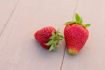 Close-up view of two ripe strawberries on wooden background. Harvest in berry garden, seasonal fruits