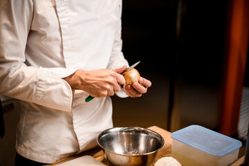 close-up of hands of male chef who peels onion with knife