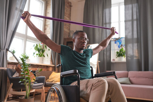 African Disabled Man Sitting In Wheelchair Raising His Arms And Doing Stretching Exercises During Sports Training At Home