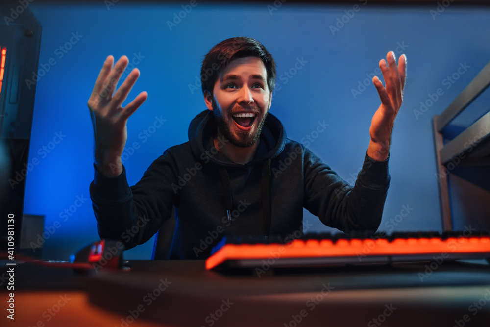 Wall mural portrait of male professional gamer won the online video game, keeps his hands up, exited, happy wit