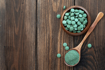Green algae in powder and pills - chlorella, spirulina on a wooden background. Healthy green food supplement concept.