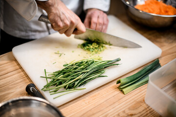 Male hands chopping salad scallion ingredient. Chef cutting green onion with sharp knife.