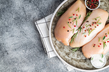 Raw uncooked chicken breasts with spices and herbs on gray concrete table, chicken meat with ingredients for cooking. Top view.