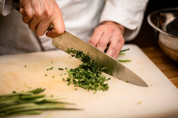 Close-up of hands of chef chopping green onion with knife on cutting board